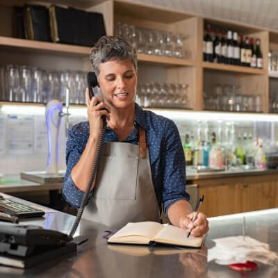 Gérante d'un restaurant qui note une réservation faite par téléphone.